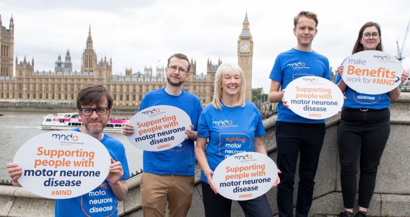 Five members of MND Association staff stand in front of the Palace of Westminster, holding signs that say ‘Supporting people with motor neurone disease’.