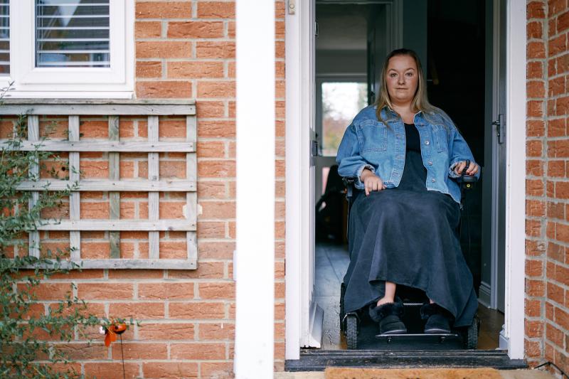Charlotte is sitting in her wheelchair inside the front door of her house, looking out