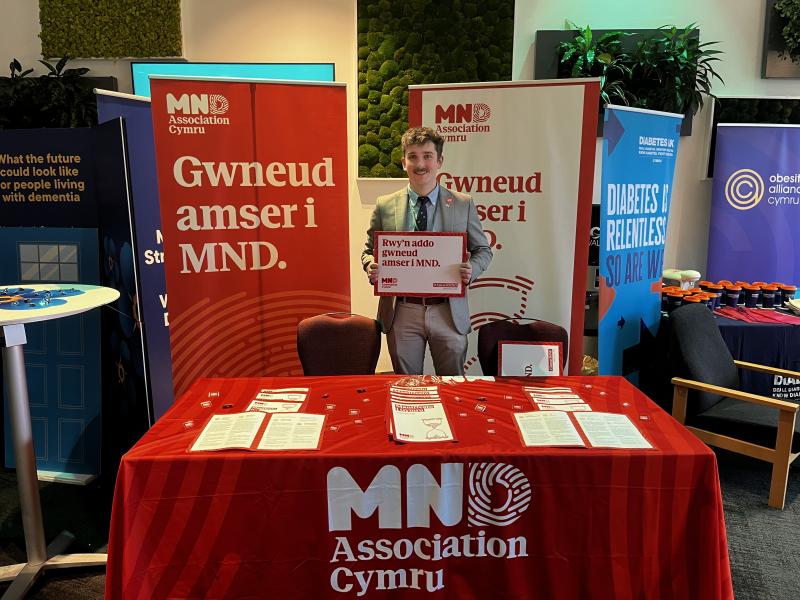 A man stands at a stall with Amser i MND branding.